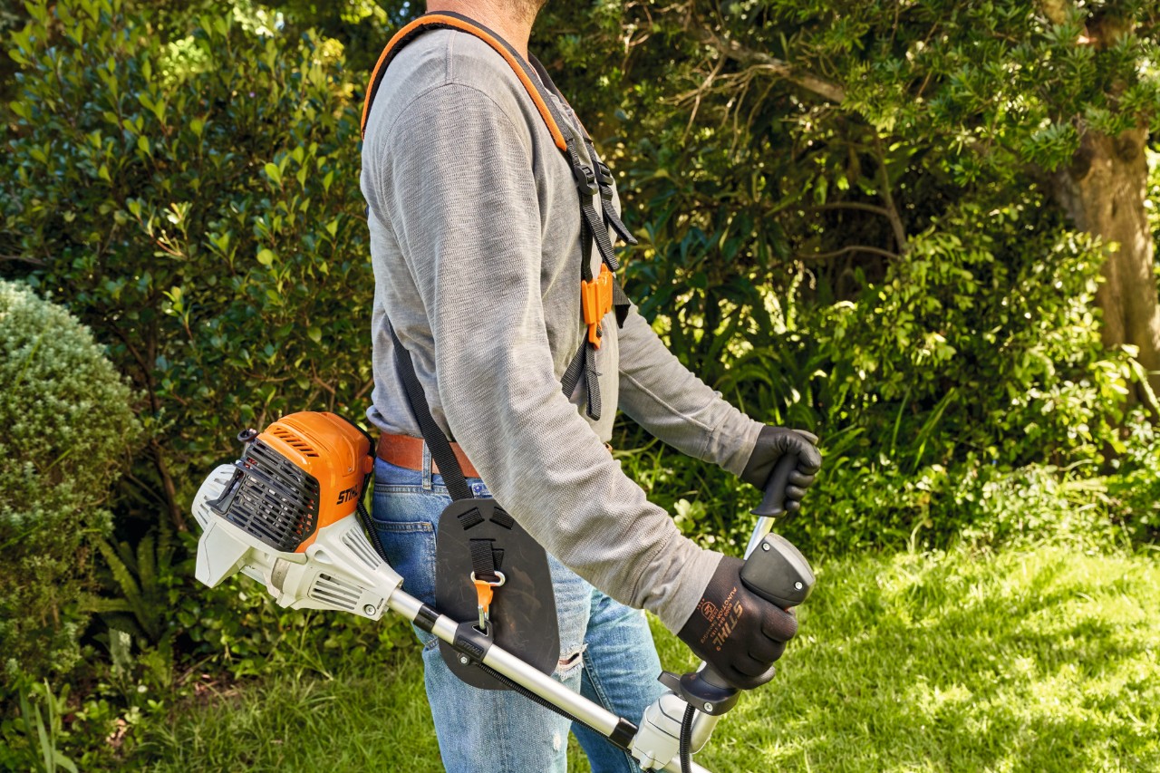 A man picking up a STIHL FS 91 petrol brushcutter from the ground to start mowing 