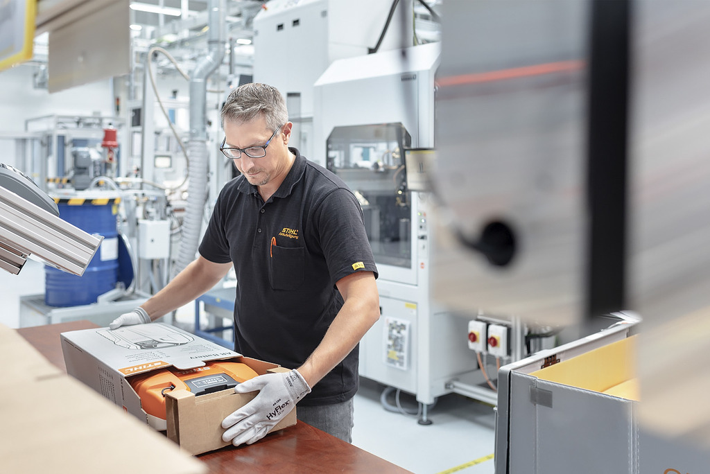An employee in battery production packs a STIHL cordless power tool into a cardboard box 
