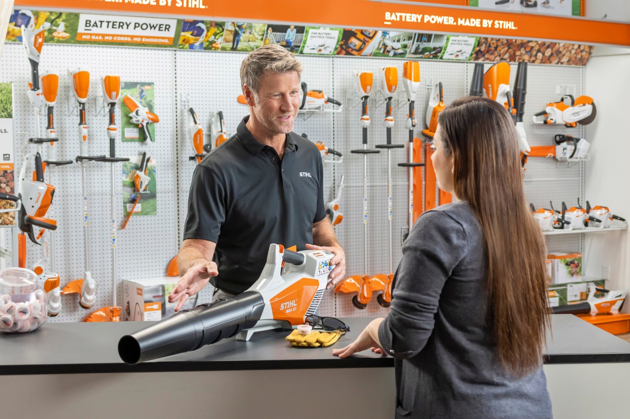 STIHL dealer advising a young woman about a STIHL hedge trimmer in front of a store shelf