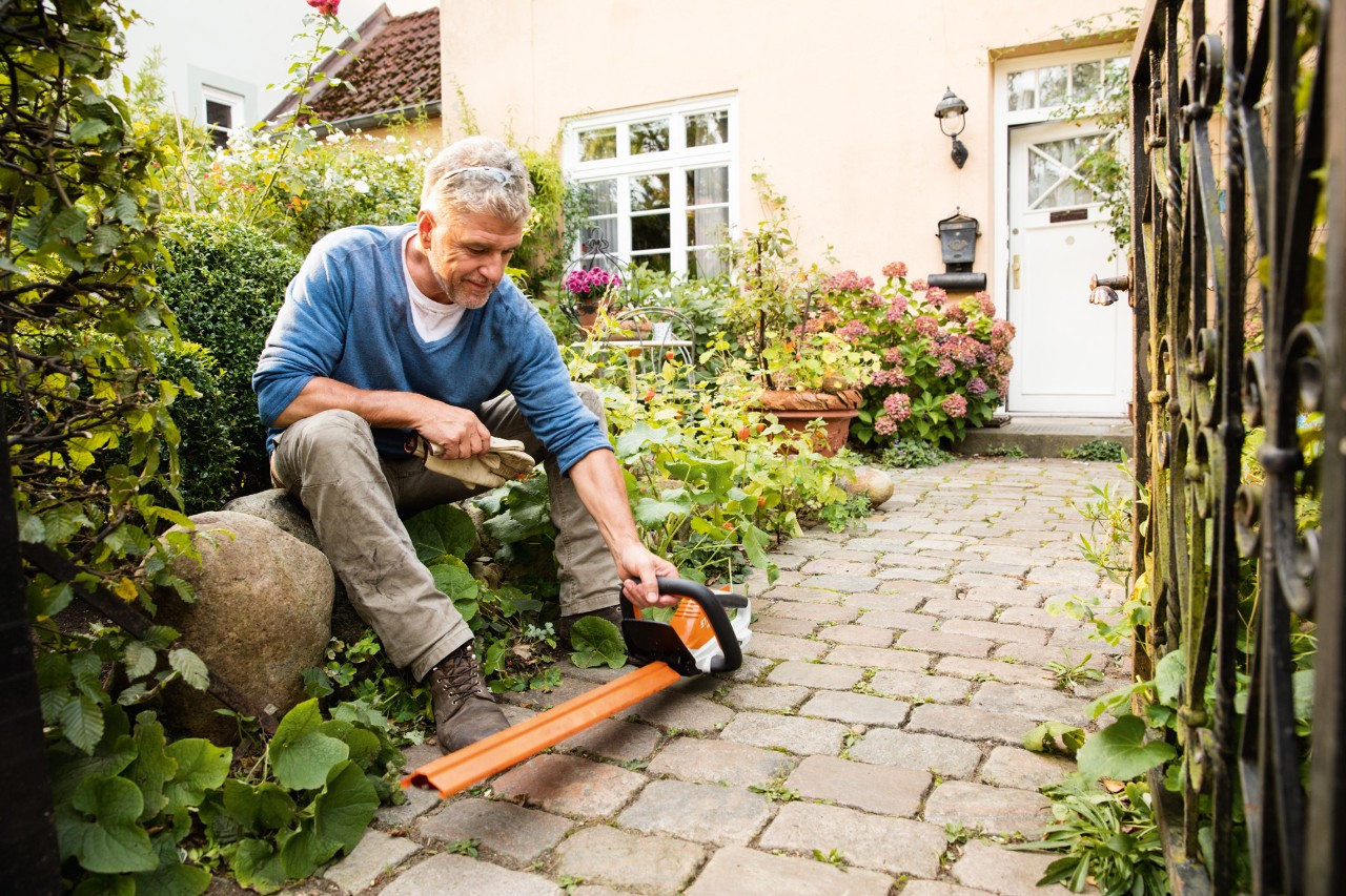 A man sitting on a large rock with STIHL AI Series electric hedge trimmer HSA 45 in front of a house